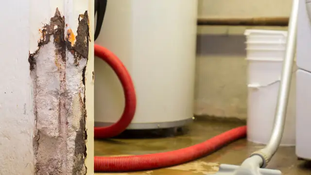 Wet vacuum hose pulling water from the floor beside a corroded post and a water heater